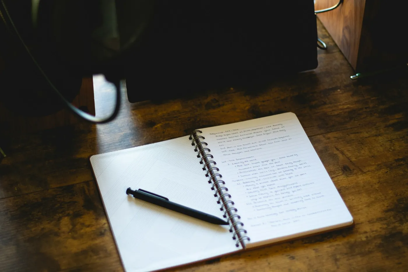An open notebook and a pen on a wooden desk by a lamp
